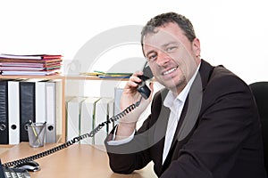 young successful man is talking on the phone at the office workplace desk wearing suit wear