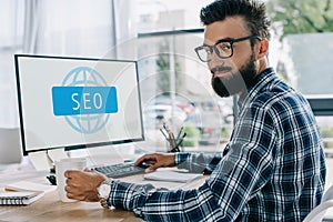 young successful seo manager sitting at workplace with computer and looking
