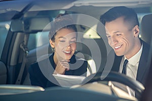 Young successful woman and man reviewing documents in car