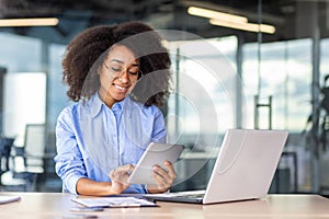 Young successful woman working with tablet computer inside office at workplace, smiling female programmer testing new