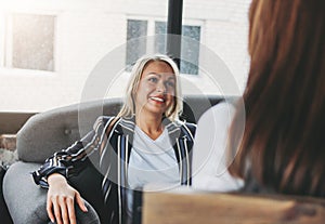 Young successful women colleagues discuss joint project, coaching or psychotherapy in modern loft office