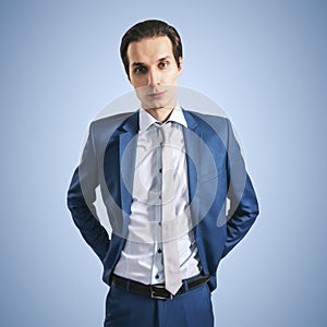 Young successfull businessman in suit and grey tie on blue background, close up