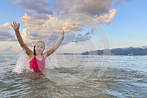 Young summer girl in pink swimsuit having fun in sea with water splash. Happy child on beach in sea on summer holidays