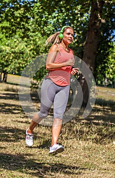 Young suntanned woman running with green headphones on