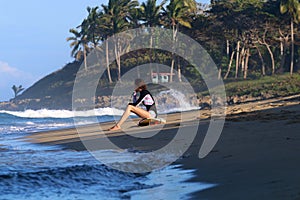 Young surfer girl sitting on the beach during sunset