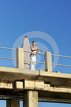 Young surfer girl standing on pier with surfboard