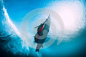 Young surfer girl with surfboard dive underwater with fun under big ocean wave.