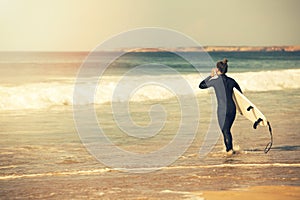 young surfer girl wearing wetsuit going into the ocean