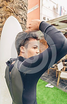 Young surfer man with surfboard closing wetsuit