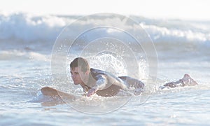 Young surfer swimming in the ocean and getting ready to catch th