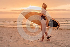 Young surfer woman with sporty body posing on beach at sunset or sunrise. Attractive surfgirl with surfboard