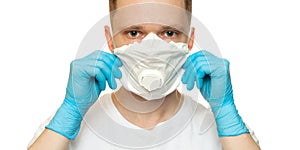 Young surgeon doctor in latex protective gloves puts on white protection mask on white background. Man in medical gloves and on