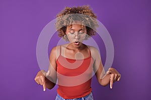 Young surprised African American woman teen points finger down stands in studio