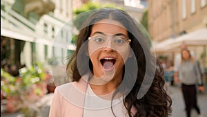 Young surprised amazed excited woman Indian Arabian female girl outside. Positive businesswoman shock smiling open mouth