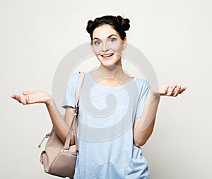 Young surprised brunette woman wearing blue t-shirt with backpack over grey background
