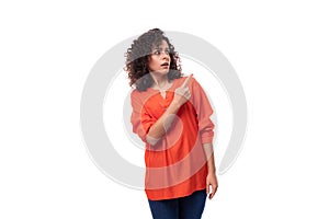 young surprised european woman with curly black hair holding dressed in a bright orange blouse on a white background