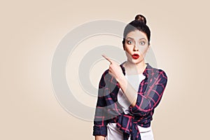 Young surprised girl with casual style and bun hair pointing her finger sideways