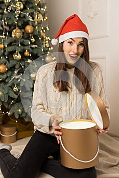 The young surprised girl holds gold gifts near Christmas festive tree