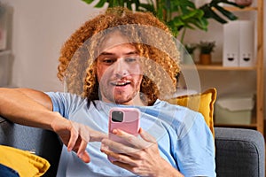 Young surprised Latin man using his phone laying on the sofa at home.