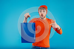 Young surprised man holds shopping bag on isolated blue background
