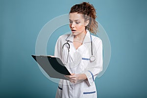 Young surprised medical nurse looking at clipboard with opened mouth