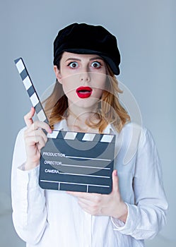 Young surprised redhead woman in hat holding movie clapboard