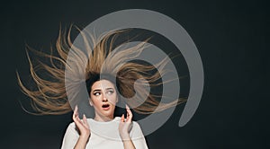 Young surprised woman with long hair lying on black background, female face expression of shock and delight top view