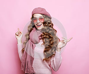 Young surprised woman with long wavy hair wearing pink shirt, eyewear and beret over pink background