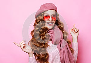 Young surprised woman with long wavy hair wearing pink shirt, eyewear and beret over pink background