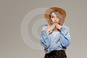 Young surprised woman model in a fashionable hat and denim jacket on a gray background.