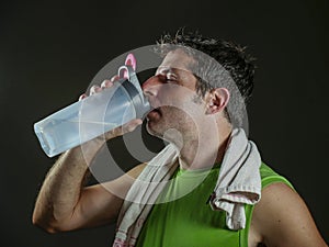 Young sweaty attractive and fit sport man drinking water holding bottle cooling off after hard fitness workout at gym club