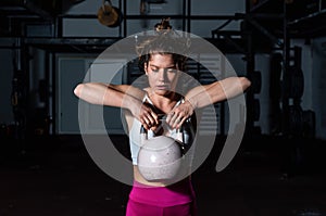 Young sweaty fit muscular strong girl doing hardcore cross workout training for shoulder muscles with heavy kettlebell in the gym