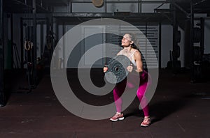 Young sweaty muscular strong fit girl holding big heavy barbell weight plate with her hands and lifting it up as hardcore cross wo