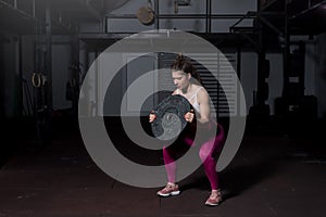 Young sweaty muscular strong fit girl holding big heavy barbell weight plate with her hands and lifting it up as hardcore cross wo