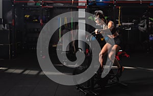 Young sweaty strong athlete woman riding or cycling air bike in the gym for strength and conditioning as heavy hardcore cardio