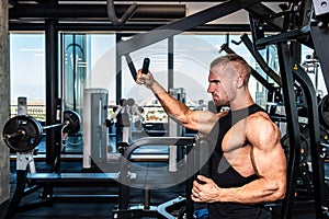 Young sweaty strong muscular fit bodybuilder man back muscles workout training with weights on the machine in the gym