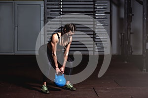 Young sweaty strong muscular fit girl holding heavy kettlebell with her hands and doing swing hardcore cross workout training in t