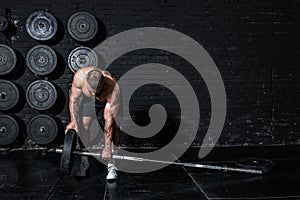 Young sweaty strong muscular fit man with big muscles putting heavy iron weight plate on the barbell for hardcore cross gym weight