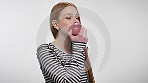 Young sweet ginger girl is biting red apple, enjoying it, white background