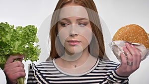 Young sweet ginger girl is choosing between healthy and unhealthy food, choose lettuce, white background