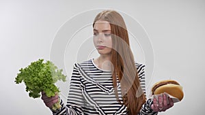 Young sweet ginger girl is choosing between lettuce and burger, green choice, white background