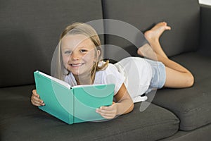 Young sweet and happy little girl 6 or 7 years old lying on home living room sofa couch reading a book quiet and adorable in child