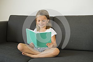Young sweet and happy little girl 6 or 7 years old sitting on home living room sofa couch reading a book quiet and adorable in chi