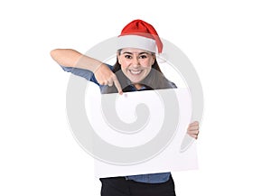 Young sweet Latin woman in Santa Christmas hat pointing blank billboard