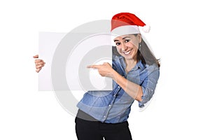 Young sweet Latin woman in Santa Christmas hat pointing blank billboard