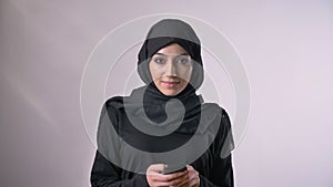 Young sweet muslim girl in hijab is typing message, communication concept, religious concept, grey background