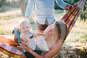 Young sympathetic family - mom, dad and son rest in the nature, sitting in a hammock