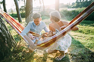 Young sympathetic family - mom, dad and son rest in the nature, sitting in a hammock