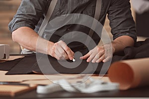 Young tailor marking fabric with chalk in atelier