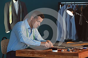 Young tailor marking fabric with chalk in atelier